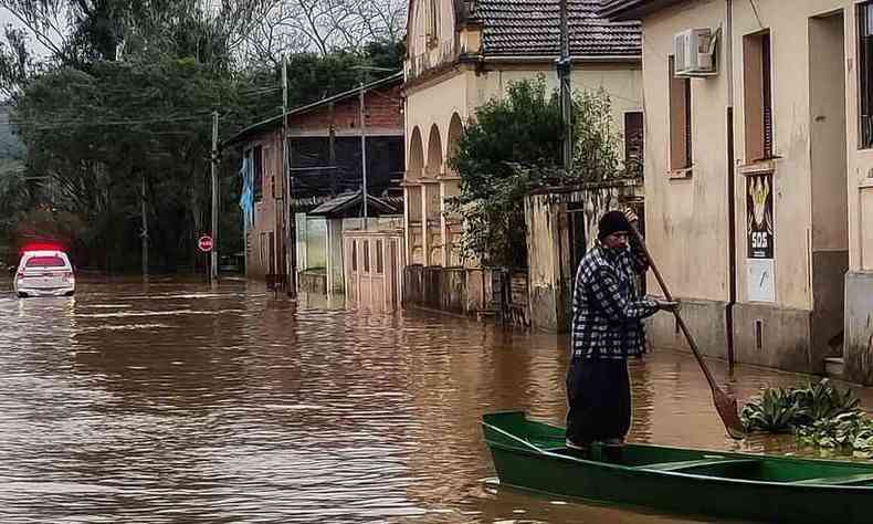 homem de barco pela rua de uma cidade no RS atingida pelo ciclone