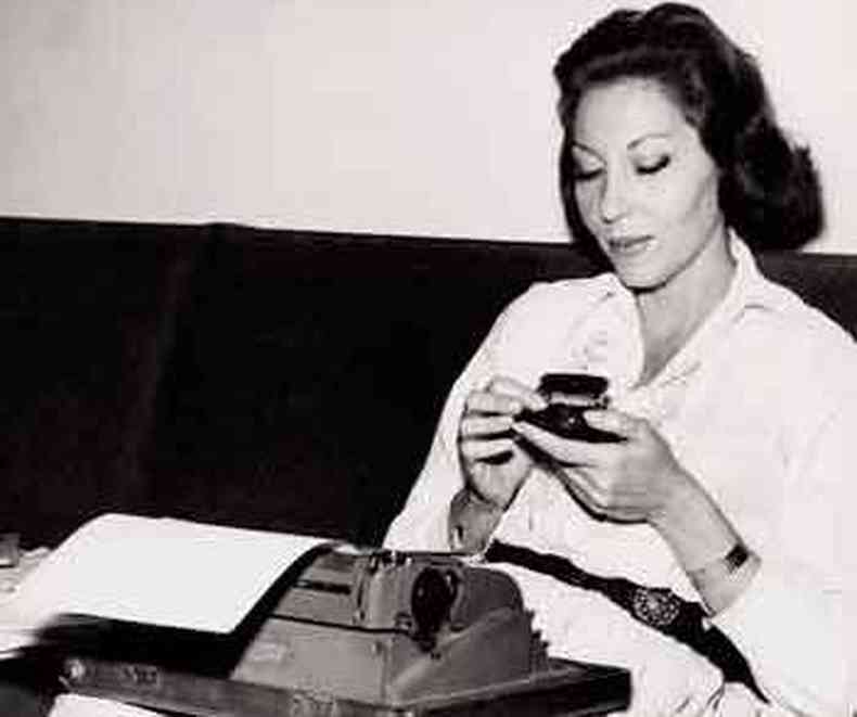 Sentada num sof, Clarice Lispector segura xcara de caf, tendo no colo uma mquina de escrever