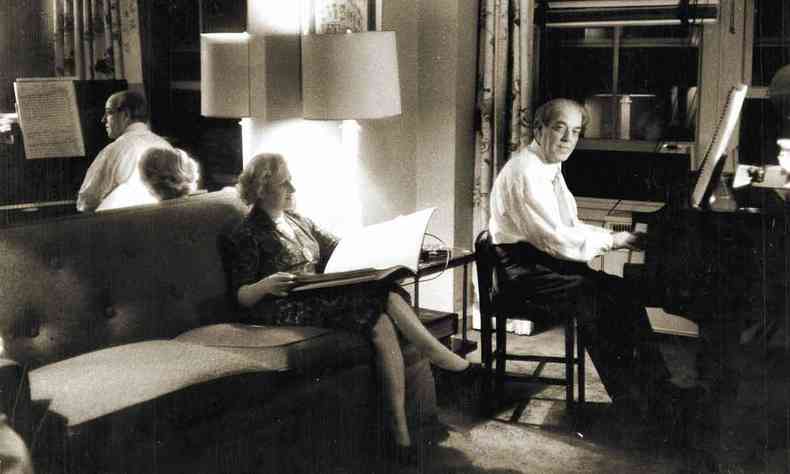 Villa-Lobos toca piano em sua casa. Sentada no sof, mulher ouve a apresentao