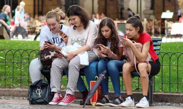 meninas usam celular sentadas em um banco de uma praa