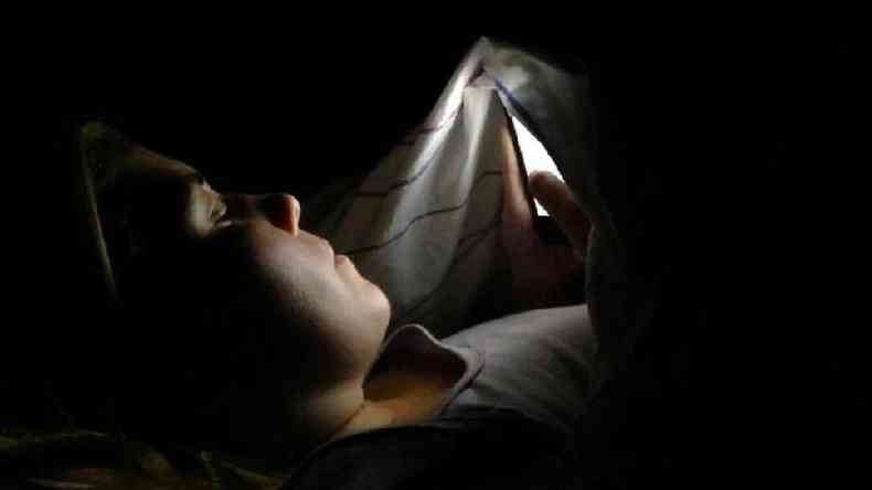 Mulher mexendo no celular no escuro