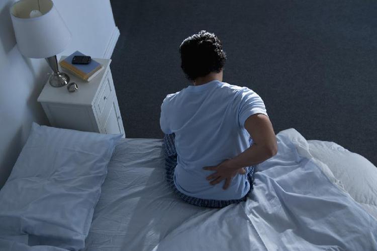Pessoa sentada na cama tocando a lombar com a mo