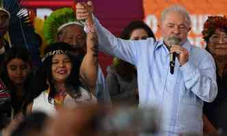 No Acampamento Terra Livre, em Brasília, Lula discursa enquanto ergue a mão de uma jovem indígena ao alto.