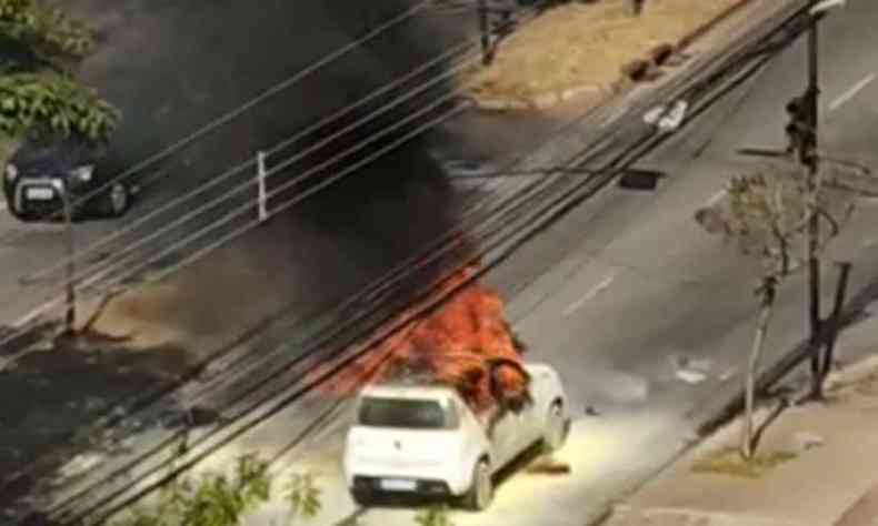 Vista do alto de um Fiat Uno branco em chamas em meio a uma fumaa escura 