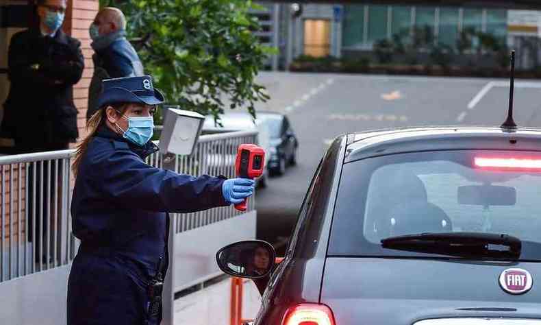 Agente de segurana (L) mede temperatura corporal de funcionrio da Fiat, que chega de carro  fbrica em Turim, na retomada do trabalho nesta segunda-feira (27-04)(foto: Miguel MEDINA / AFP)