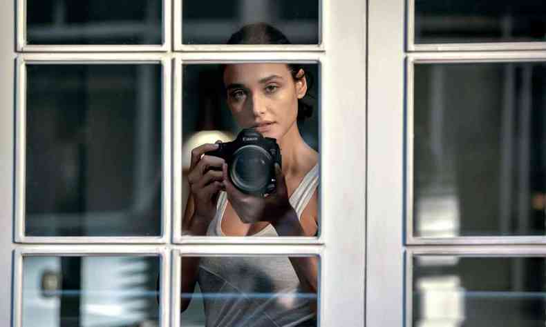 A atriz Dbora Nascimento segura cmera atrs de janela em cena de 'Olhar indiscreto' 