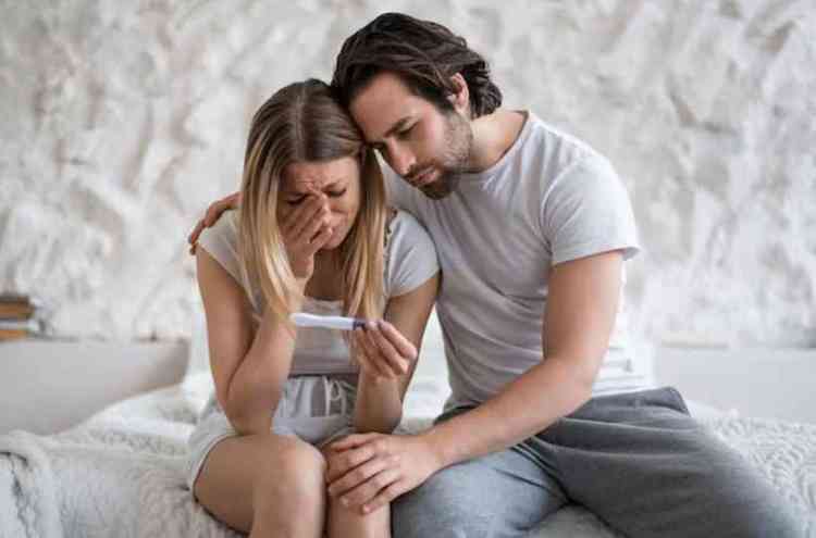 Jovem chateada com teste de gravidez negativo chorando na cama com marido apoiando-a