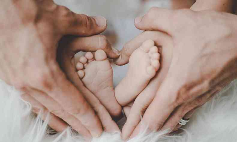 pés do bebê envolvido pelas mãos do pais formando um coração