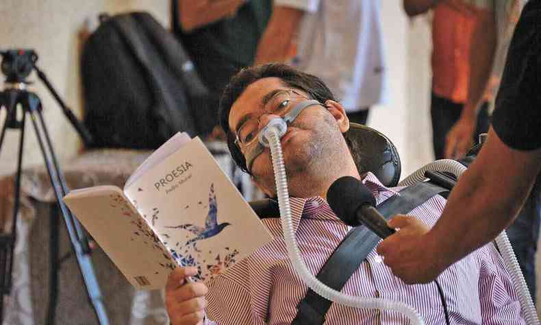 Sentado em cadeira de rodas, o escritor Pedro Muriel segura volume do livro 'Proesia'