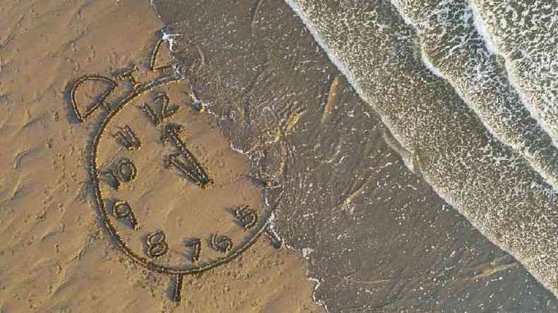Praia com relgio desenhado na areia