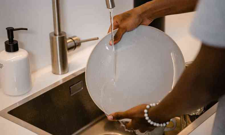 Mãos de uma pessoa negra lavando um prato