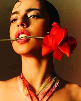 A cantora Marina Sena, de cabelos presos, tem uma rosa entre os dentes 