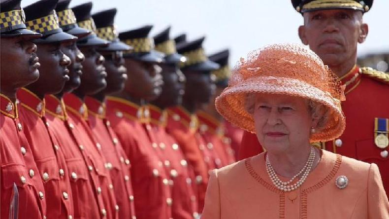 O legado colonial do Reino Unido coloca a monarquia sob escrutínio(foto: Getty Images) A rainha Elizabeth, uma senhora branca idosa de terno e chapéu rosas, passa em frente a vários homens negros fardados em uma visita à Jamaica em 2002