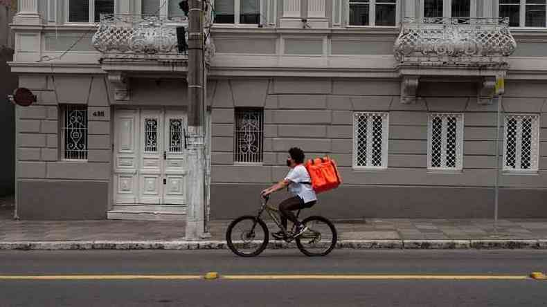 Franciele de bicicleta pedalando na rua, com mochila de delivery