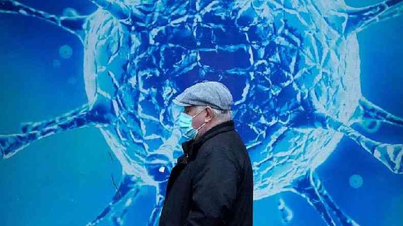 Homem com máscara passa diante de mural ilustrado com um coronavírus
