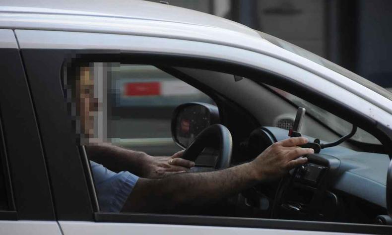 Na foto, motorista mexe no celular dentro de carro