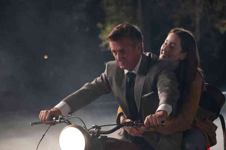 O ator Sean Penn dirige motocicleta  noite com a atriz Alana Haim na garupa em cena de Licorice Pizza 
