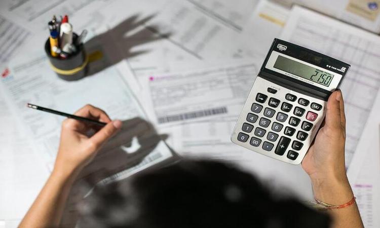 homem segurando calculadora, um lpis e uma messa cheio de boletos