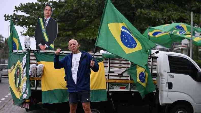 Apoiador do presidente Jair Bolsonaro carregando bandeira do Brasil, em frente a um pequeno caminho tambm decorado com bandeiras, bonecos inflveis de Lula vestido de presidirios e uma imagem de Bolsonaro em papelo