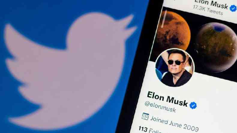 Celular mostra o perfil de Elon Musk no Twitter com o logotipo da plataforma ao fundo