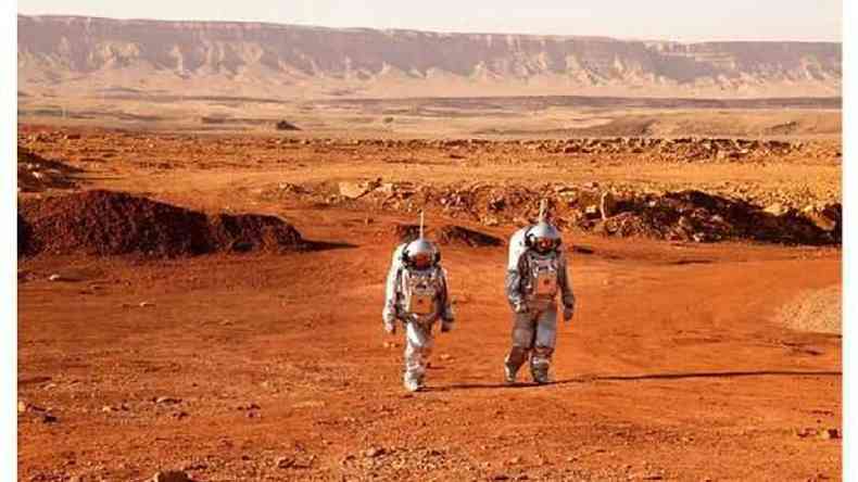 Dois homens com roupas prateadas de astronautas andam em um deserto laranja que lembra a superfcie de Marte