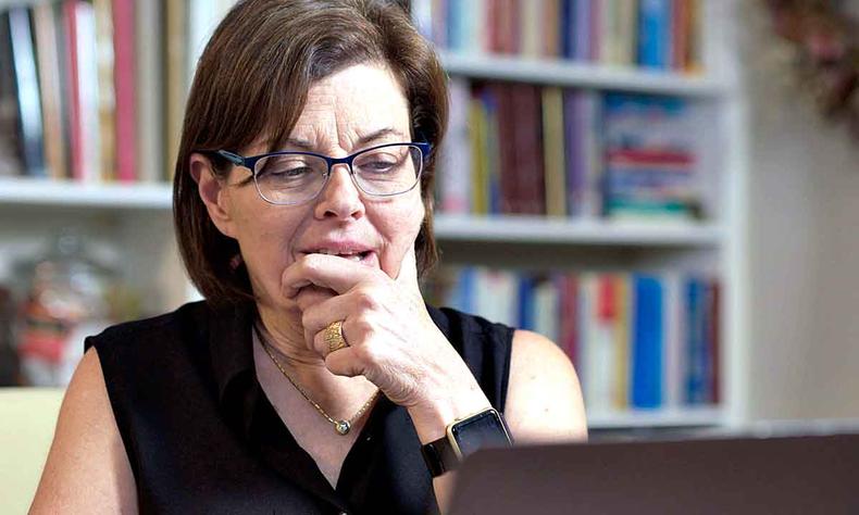 De culos e com o queixo apoiado na mo esquerda, Nancy Salzman olha para tela de computador 