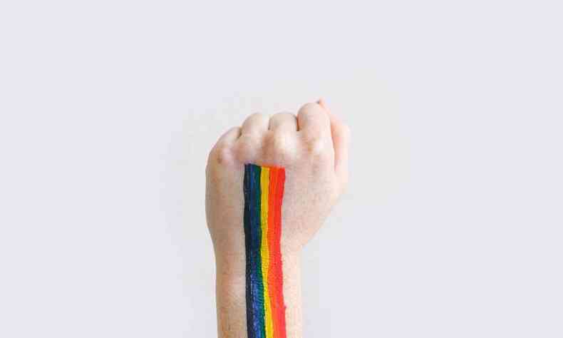 Mo em punho de uma pessoa branca com as cores da bandeira LGBTI