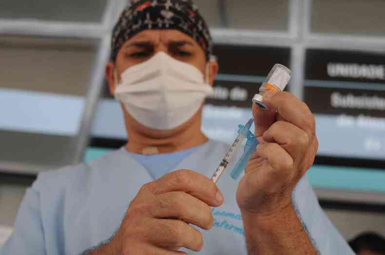 Enfermeiro segura seringa e frasco do imunizante prepara a aplicao da vacina.