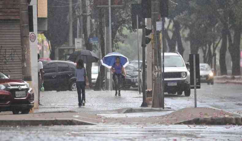 Chuva intensa, pessoa anda com guarda-chuva em cruzamento.