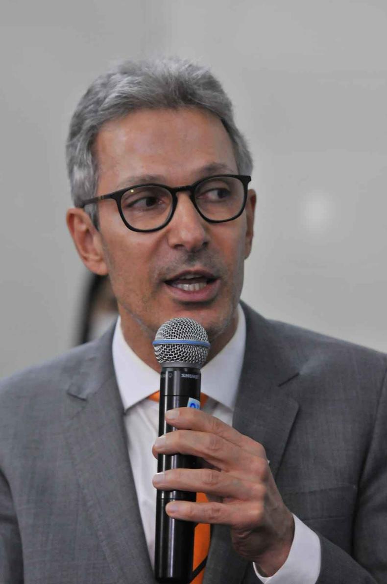 Governador Romeu Zema fala ao microfone em fundo branco