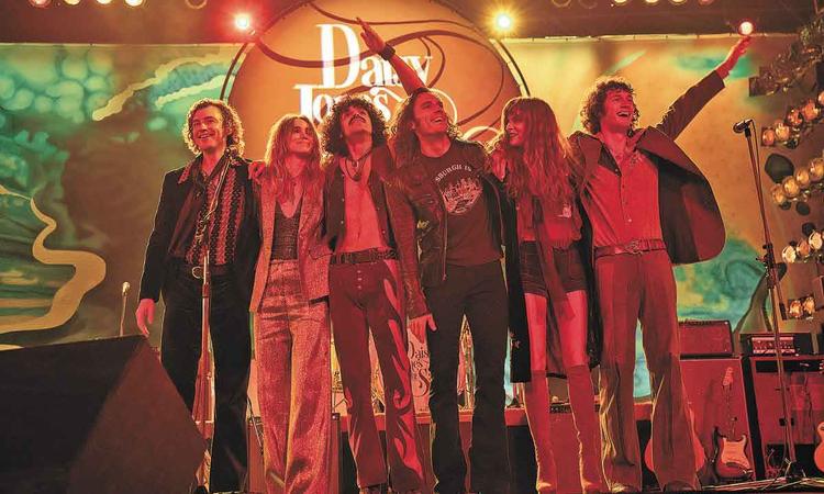 Atores da banda Daisy Jones & The Six abraados no palco, em cena da srie homnima