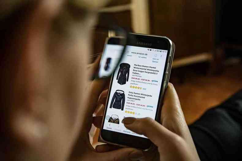 Mulher olha site de vendas de roupas em telefone celular