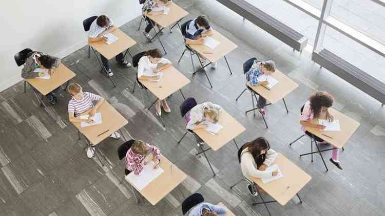 Foto tirada do alto mostra vrias crianas fazendo atividade com papel em suas carteiras da escola