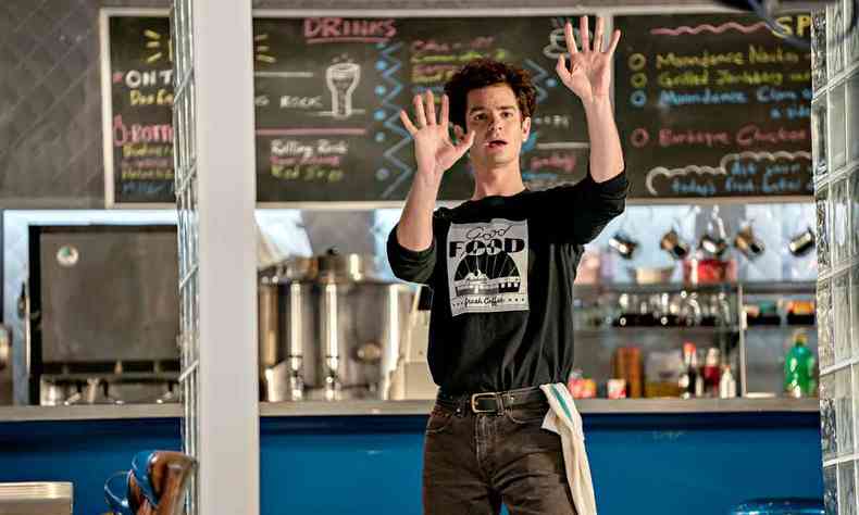 O ator Andrew Garfield ergue as mãos num restaurante em cena de tick tick boom