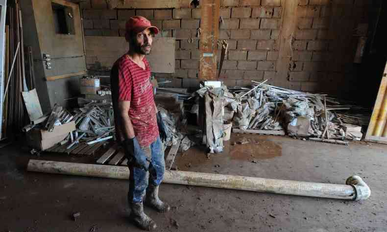 homem de blusa e bonés vermelhos mostra estrago dentro de depósito de material de construção em Brumadinho