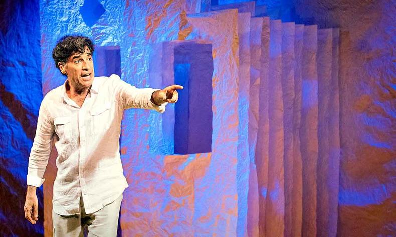 Vestido de branco, Paulo Betti gesticula no palco, em cena de 'Autobiografia autorizada'