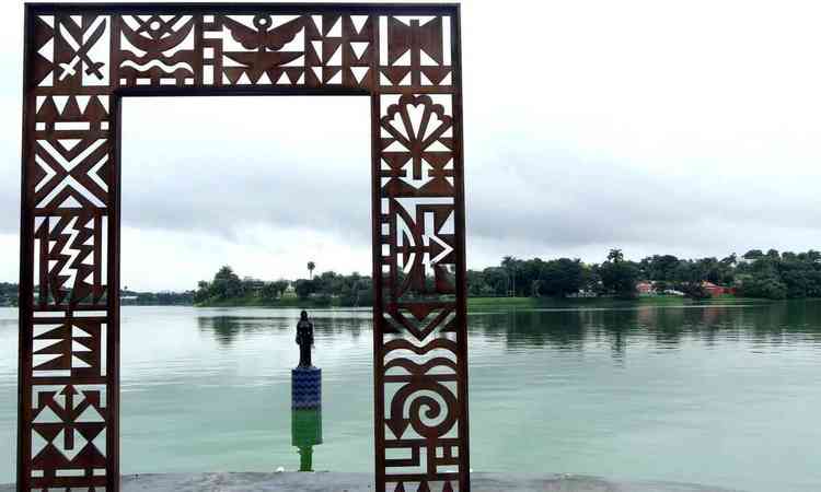 Foto mostra o Portal da Memória, com Iemanjá embaixo da escultura e, ao fundo, a Lagoa da Pampulha, em BH