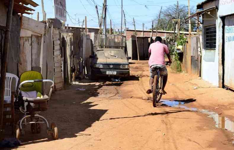 Homem pedala em via de terra em favela de Braslia