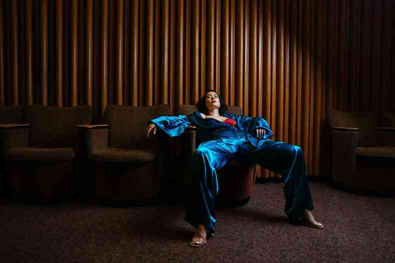 A cantora nipo-americana Mitski est quase deitada em um sof vestido cala e blusa azuis 