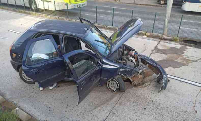 Foto do acidente com o carro, um Fiat Pálio azul escuro, destruído