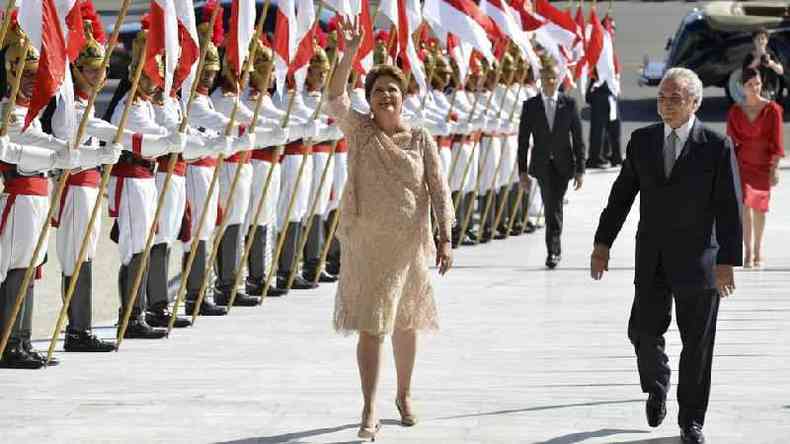 Dilma Rousseff e Michel Temer sorriem caminhando em corredor formado por drages (guardas)