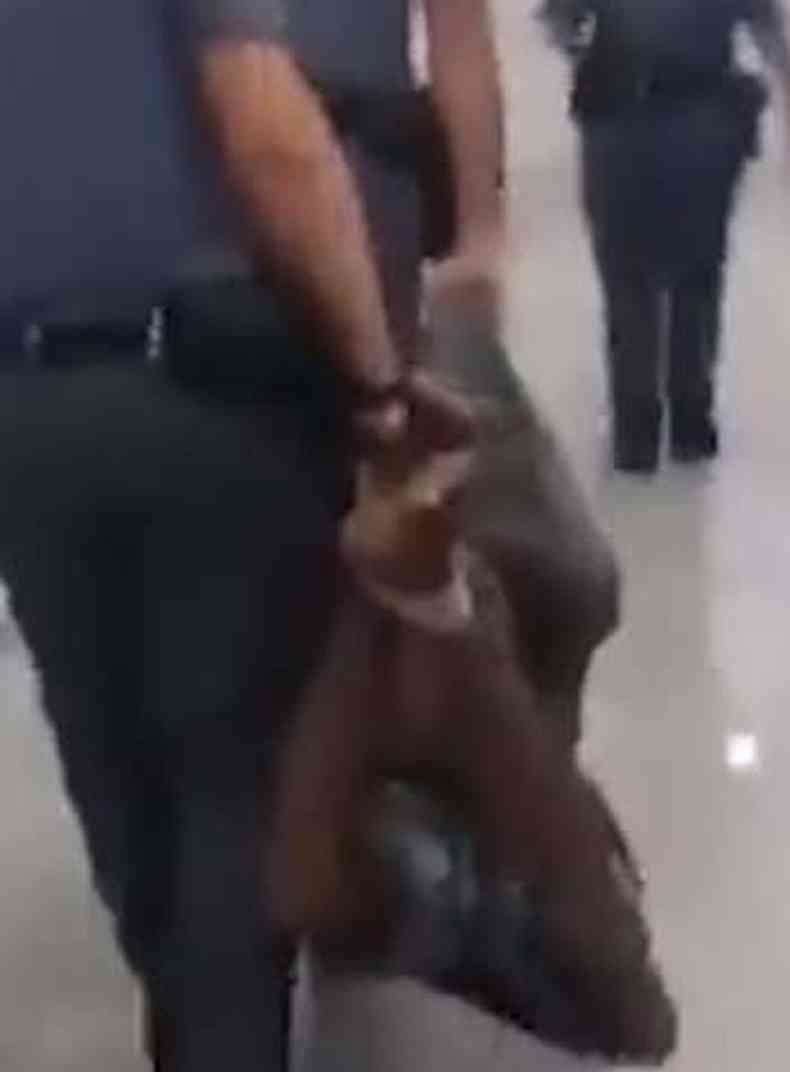 Imagem do homem sendo carregado pelos pés e mãos por policiais