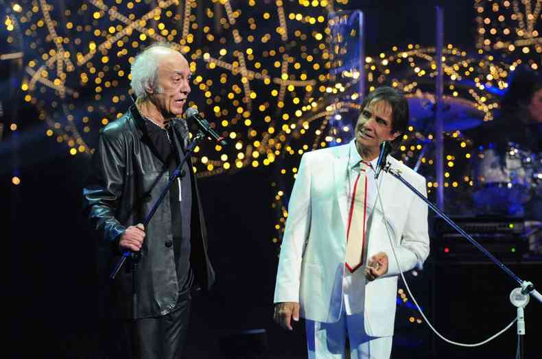 Erasmo Carlos com roupa preta e Roberto Carlos com roupa branca se apresentando juntos no palco