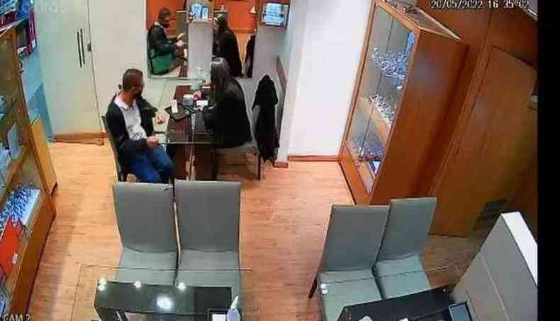 Imagens do circuito de segurana da loja mostra homem sentado  mesa em frente a uma vendedora
