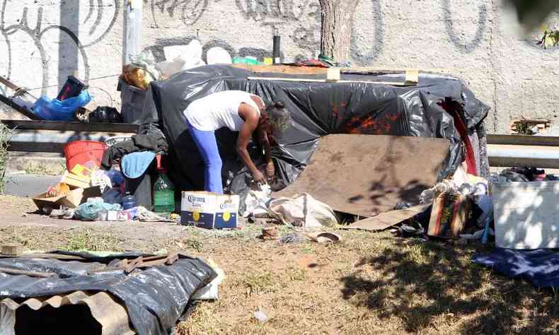 foto mostra pessoa em situao de rua em frente a barraca improvisada de lona e objetos espalhados pelo cho