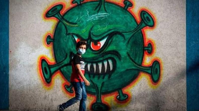 Criana caminha em frente de mural com representao do coronavrus