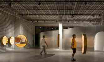 interior do centro, duas pessoas caminham e observam imagens de queijos em molduras circulares suspensas