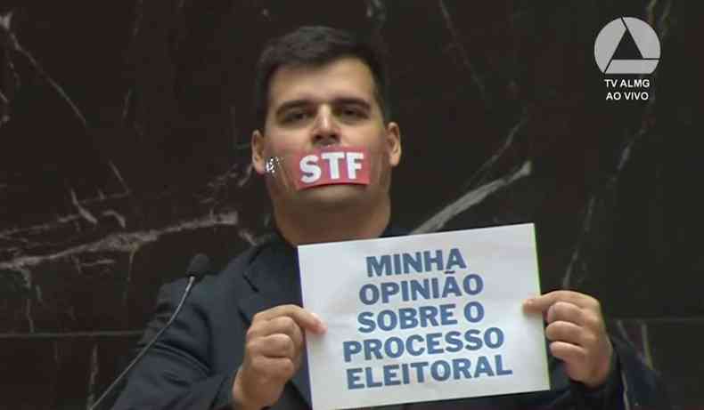 Bruno Engler com adesivo na boca escrito STF e faixa dizendo 'minha opinio sobre o processo eleitoral'.