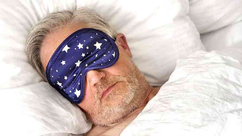 Homem na cama usando máscara para dormir