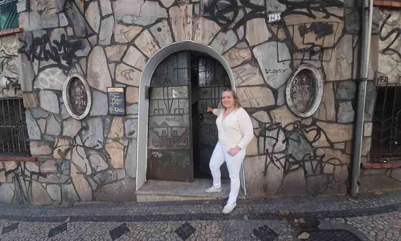 mulher vestida de branco na porta de uma casa com paredes de pedra em bh